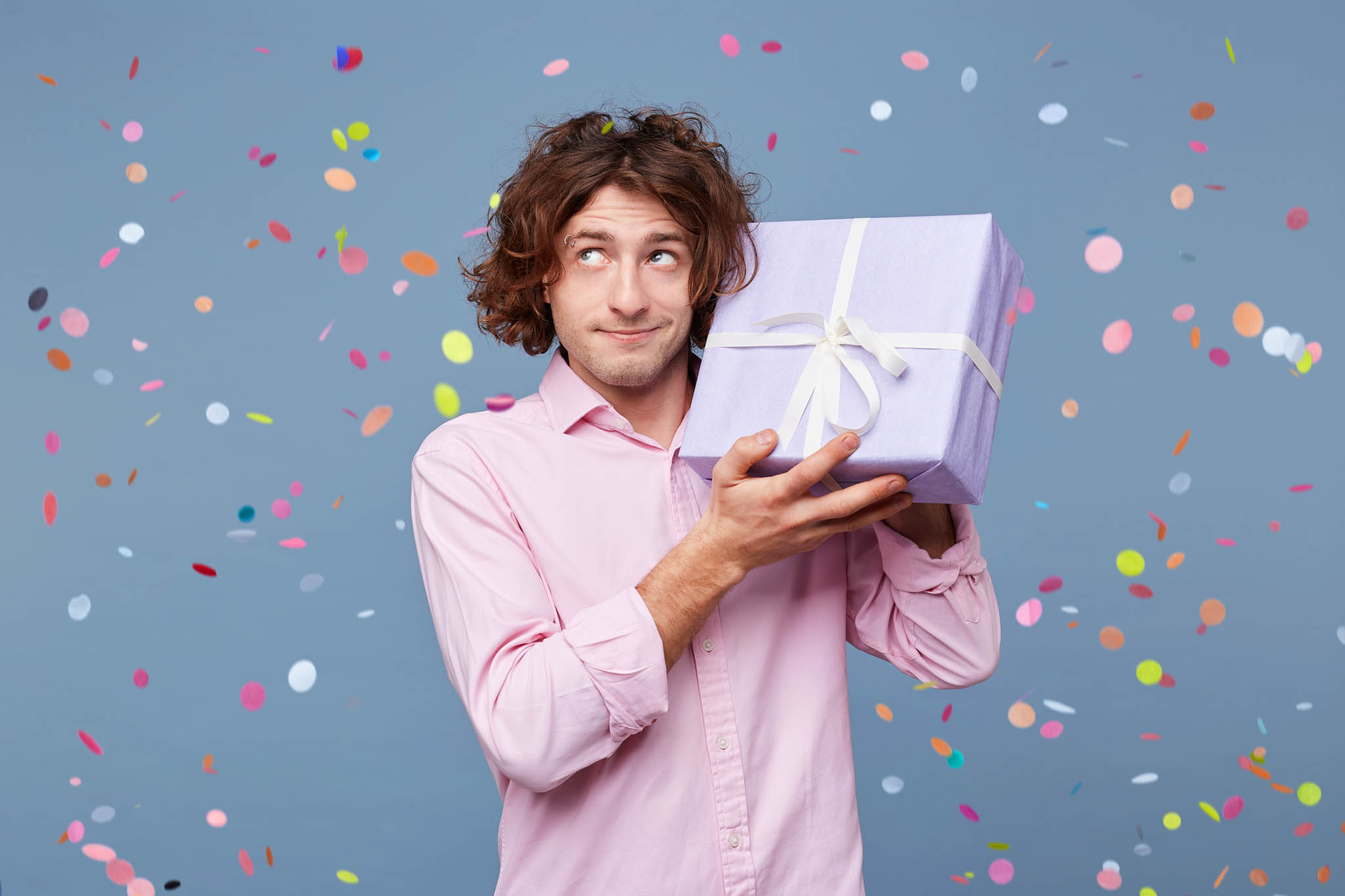 Guy on blue background holding a present with confetti falling