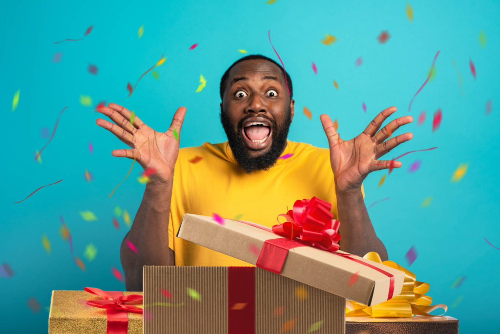 Man on teal blue background with streamers and confetti around him excited as he opens a gift