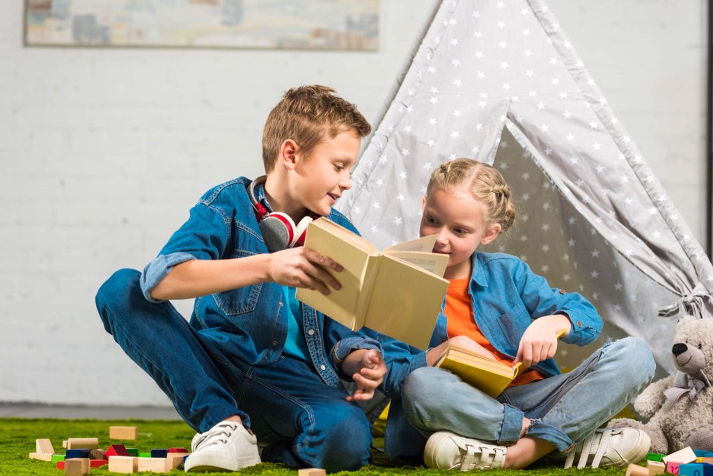 brother and sister sitting in front of a tent in a room with brother pointing something out in the book