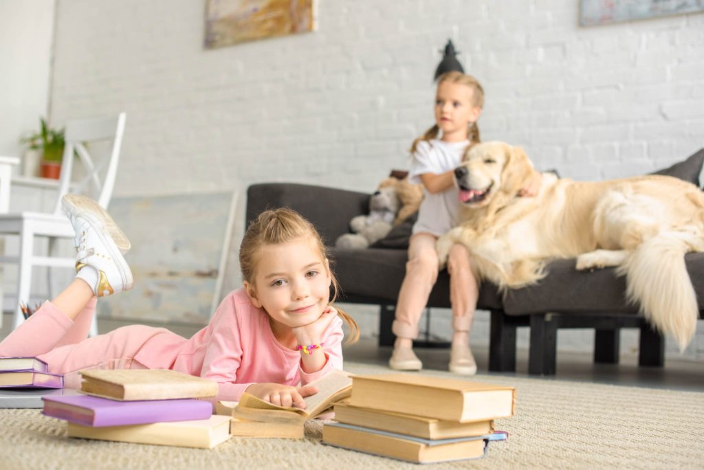 kid laying on the floor surrounded by books with a kid and dog on the couch