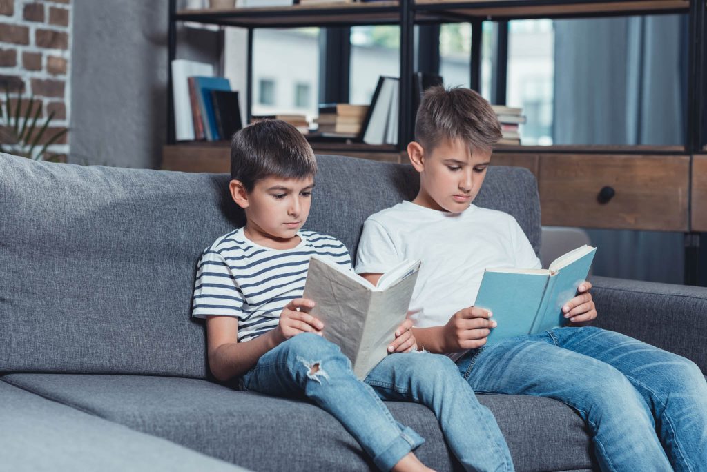two boys brothers reading on a blue couch