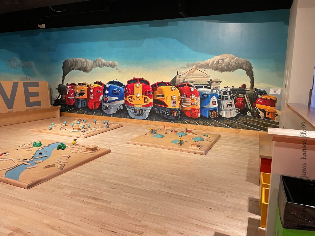 wooden train layouts for kids to play with in front of a mural