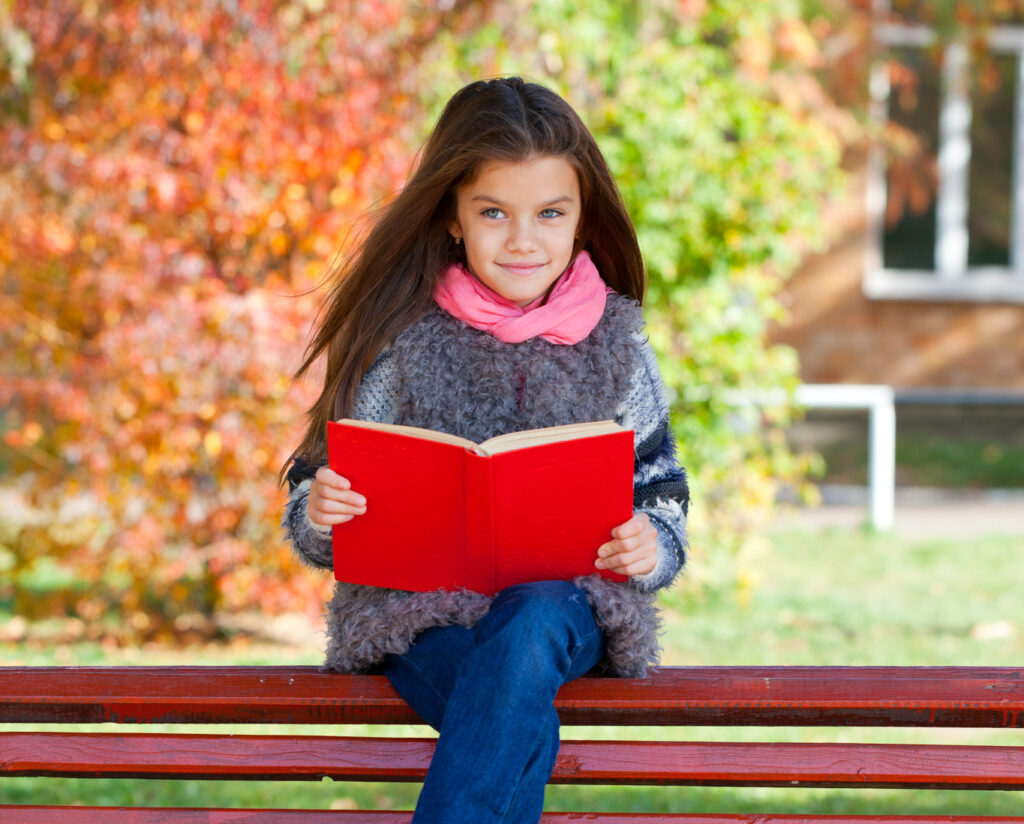 Beautiful little girl sitting on a bench in autumn park